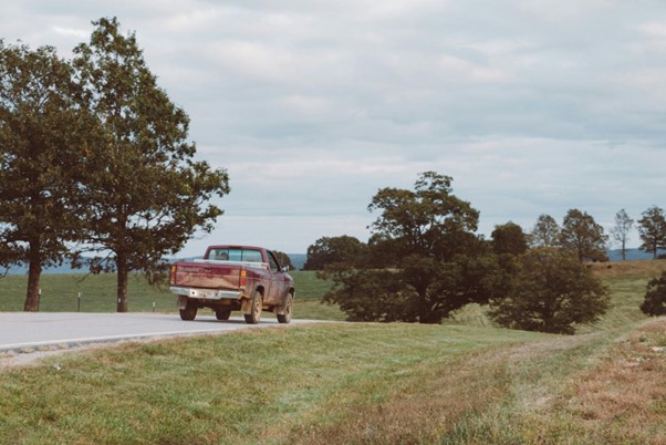 A weathered pickup truck travels along a quiet rural road