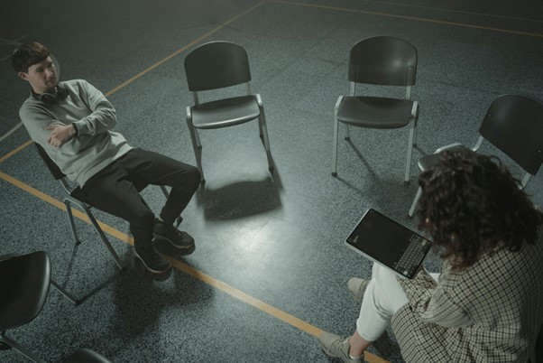 A young man and counselor sit across from each other in a group therapy setting